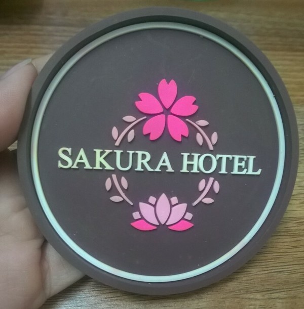 Mẫu lót ly in logo của Sakura Hotel và những bông hoa anh đào nổi bật trên nền tối 